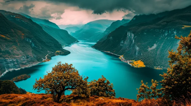 The image displays a vibrant, mountainous landscape featuring a winding turquoise fjord flanked by tall, rugged cliffs. A few trees with autumn foliage are in the foreground, and the sky above is overcast with dramatic clouds, adding a mystical feel to the scene—perfectly captured for your AI travel planner. - easytrip.ai