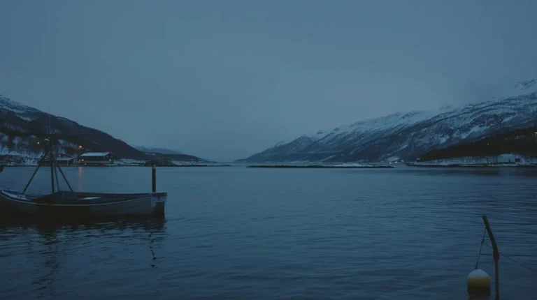 A serene twilight scene featuring a calm body of water bordered by snow-covered mountains. A lone fishing boat is anchored to the left, while a few lights from distant buildings glimmer near the shore. The sky is overcast, casting a tranquil blue hue over the landscape, perfect for an AI trip planner's next suggestion. - easytrip.ai